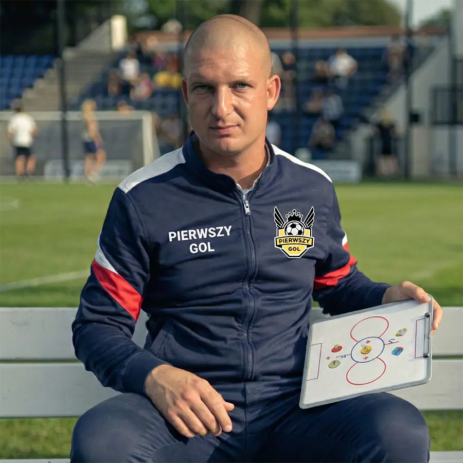 Grupa uśmiechniętych dzieci w strojach piłkarskich na zielonym boisku podczas treningu